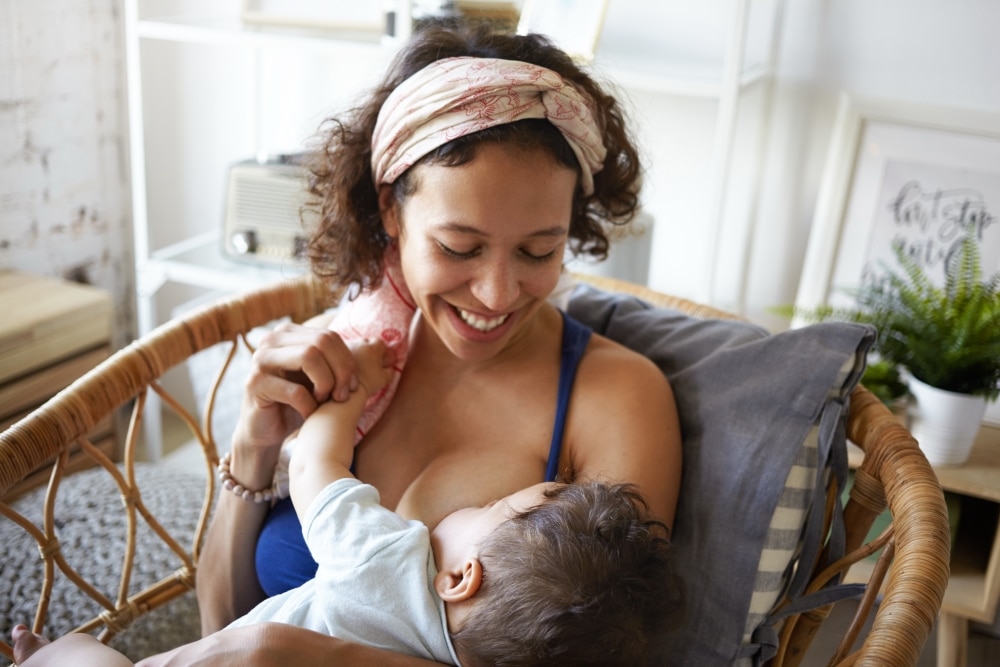 Woman smiling at her breastfeeding baby, holding baby's hand.