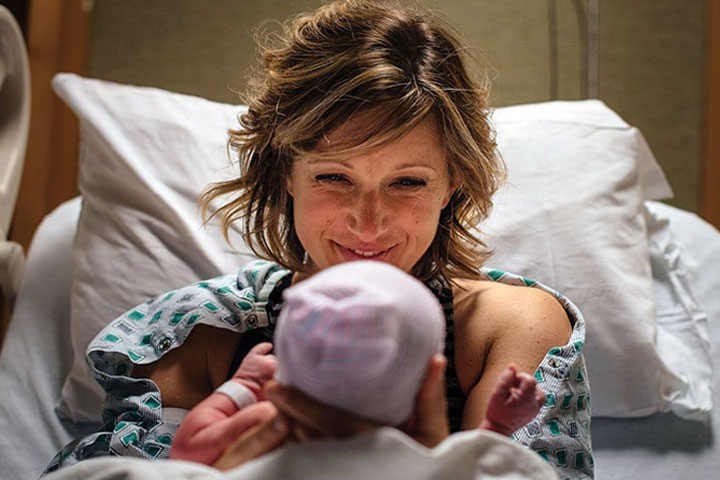 Նորածին երեխային ձեռքերի մեջ պահող և ժպտացող կին